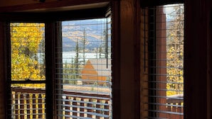A room with a view through a window with metal bars, featuring a wooden cabin and autumn foliage. - OPEN YEAR ROUND - 3 Bedroom Lake San Cristobal Condo on the Alpine Loop (Lake City)
