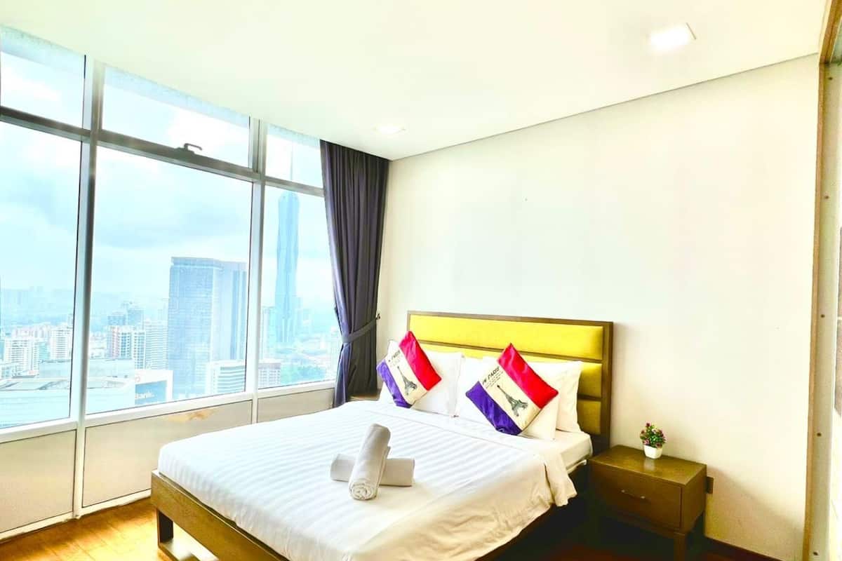 A hotel room with a large window, a bed with white linens, and a nightstand with a plant.