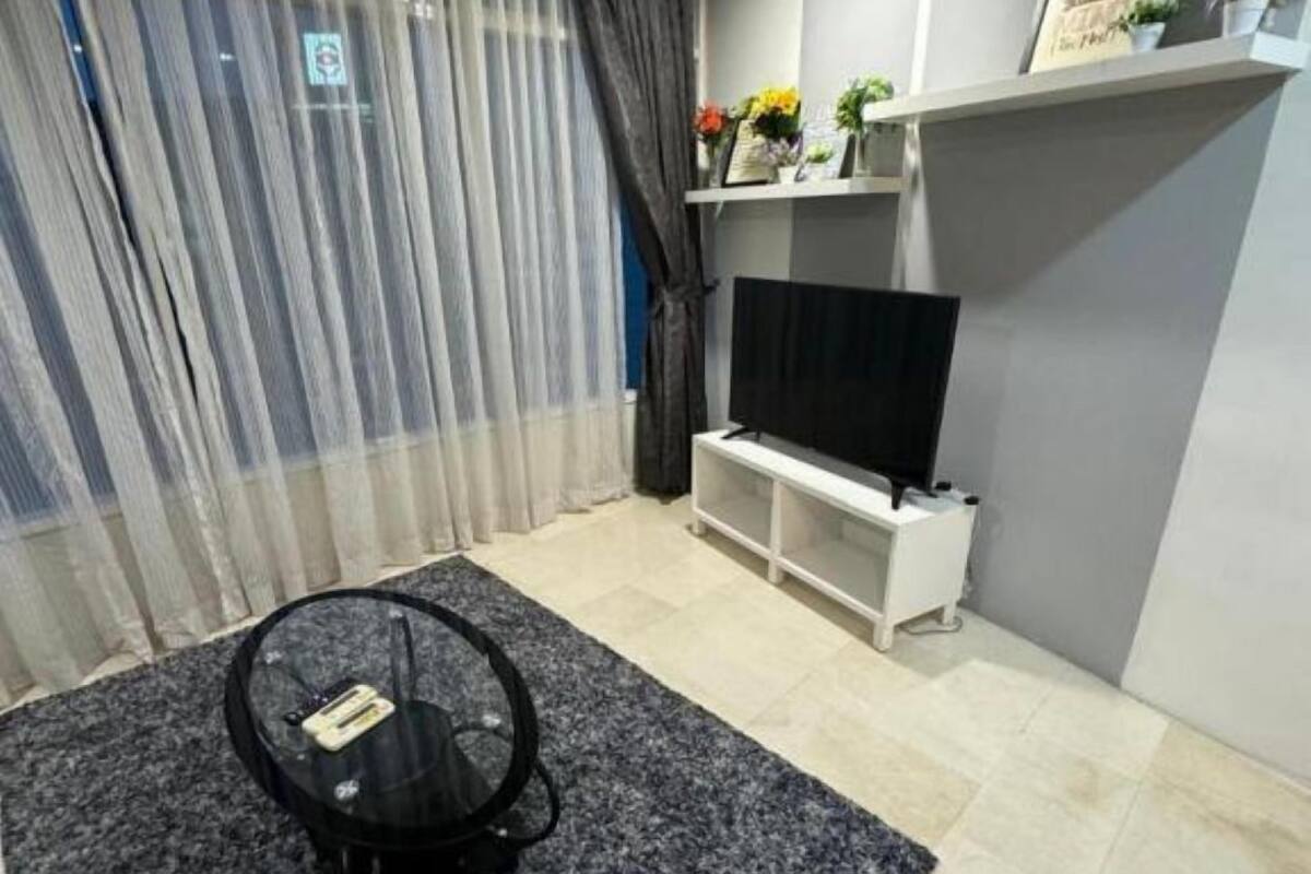 A modern living room with a flat-screen TV, a small round coffee table, and a grey carpet.