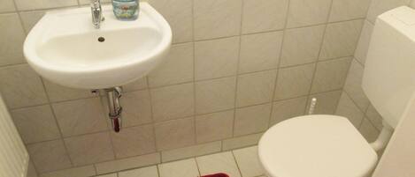 Une salle de bain avec un lavabo blanc, des toilettes et un tapis de bain rouge.
