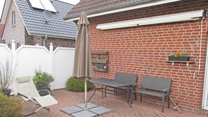 A patio with a table and chairs, a sun umbrella, and a brick wall. - Ferienunterkunft in Hagermarsch (Hagermarsch)