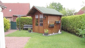 A small wooden cabin with a green roof, surrounded by a well-maintained lawn and a hedge. - Ferienunterkunft in Hagermarsch (Hagermarsch)