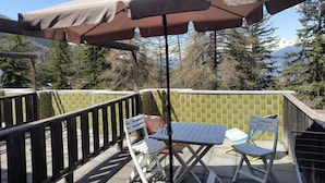 En uteplats med ett bord och stolar, ett stort parasoll och utsikt över träd och berg.