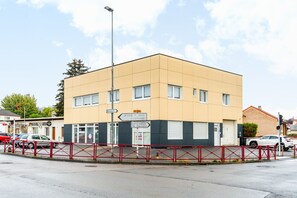 A modern building with a beige facade, multiple windows, and a red metal fence in front. - AML - Atelier Musique & Lutherie - Appt 20 min de Metz (Gandrange)