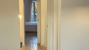 Een hal met houten vloer die leidt naar een kamer met een bed en een raam.