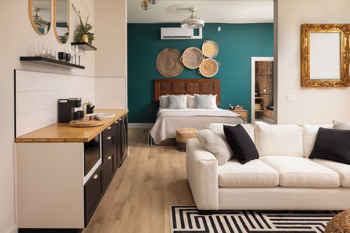 A modern bedroom with a bed, bedside table, and a view into the kitchen.