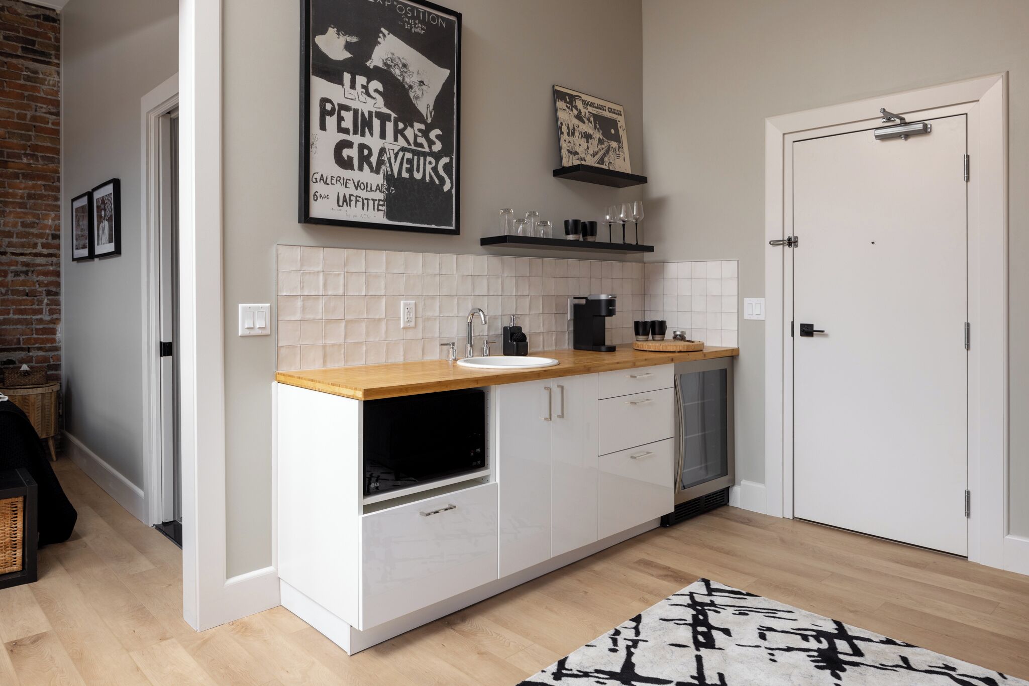 A modern kitchen with white cabinets, a wooden countertop, and a built-in dishwasher. There are two framed pictures on the wall above the counter.