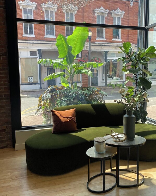 Un coin salon accueillant avec un canapé vert, une petite table ronde ornée d’une bougie et une plante en pot.