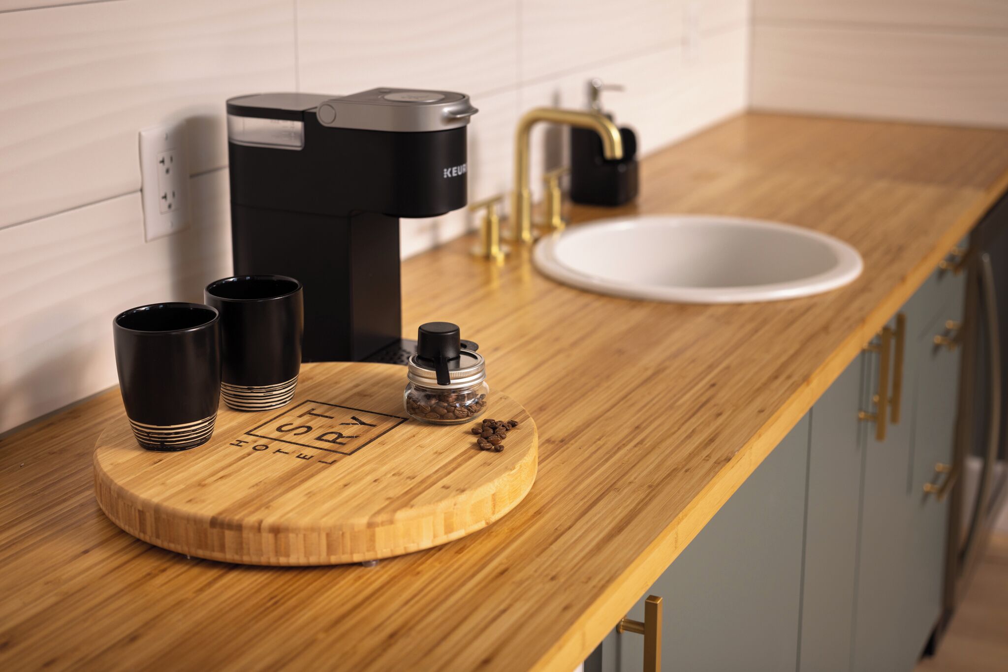 Una encimera de cocina con una cafetera, un fregadero y dos tazas sobre una tabla de madera.