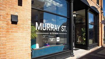 Tiilestä rakennettu rakennus, jossa on suuri ikkuna, ja ikkunassa näkyy teksti: ”MURRAY ST. KITCHEN” ja ”TELLER’S DELI”.