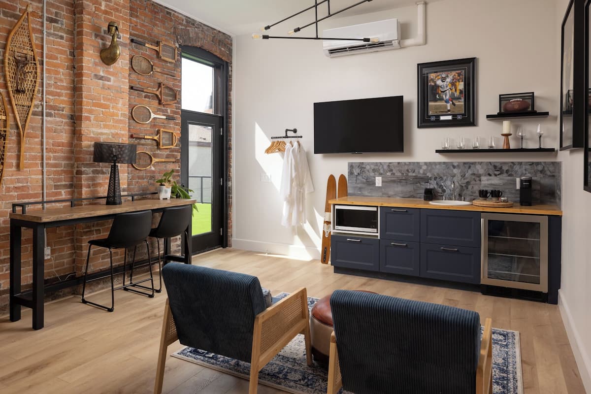A modern kitchen with a brick wall, a flat-screen TV, and a dining area with a wooden table and chairs.