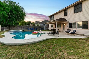 A backyard with a swimming pool, lounge chairs, and a covered patio area. - The Mad Hatter Heated Pool Gameroom  (Pflugerville)