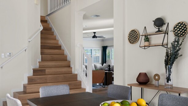 Une cuisine moderne avec un escalier en bois, un coin repas agrémenté d’un saladier de fruits, et un salon avec un canapé et une table basse.