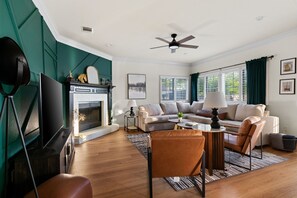 A living room with a fireplace, sofa, and television. - The Mad Hatter Heated Pool Gameroom  (Pflugerville)