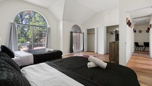 Une chambre d’hôtel moderne avec deux lits, une grande fenêtre en arc de cercle et une vue sur les arbres.