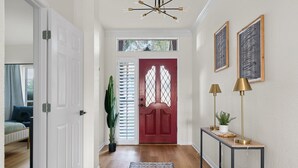Un couloir avec une porte rouge, une console surmontée de lampes et un tapis à motifs.