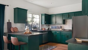 Une cuisine moderne avec des meubles de couleur turquoise, un îlot central doté de tabourets, une grande fenêtre et un réfrigérateur en acier inoxydable.