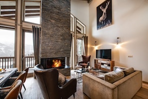 A cozy living room with a fireplace, a television, and a large window overlooking a mountainous landscape.