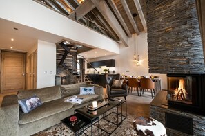 A modern living room with a fireplace, a sofa, a coffee table, and a dining area with chairs.