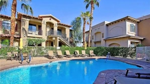 A swimming pool with lounge chairs, palm trees, and a building with balconies.