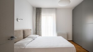 A minimalist bedroom with a bed, a door, and a window with curtains. - Santo Stefano Design Apartment by Wonderful Italy (Bologna)