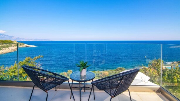 Ein Balkon mit zwei Stühlen und einem Tisch, mit Blick auf das klare, blaue Meer und eine entfernte Küste.