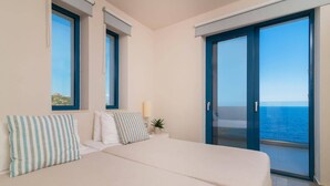 Ein Schlafzimmer mit zwei Betten, einem großen Fenster und einem Balkon mit Meerblick.