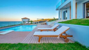 Ein Poolbereich mit Liegestühlen, einer Holzterrasse und Blick auf das Meer.