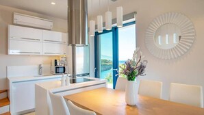 Eine moderne Küche mit weißen Schränken, einer Edelstahl-Dunstabzugshaube und Blick ins Freie durch ein großes Fenster.