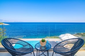 A balcony with two wicker chairs, a small table, and a potted plant, overlooking a clear blue sea and a distant coastline. - Villa Dejavu Vrahos by Villa Plus (Ionian Islands)