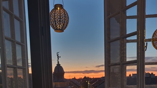 A view through open windows with a street scene, including a building with a dome and a statue. - MoMa Escape Kecskemét (Kecskemét)