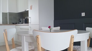 A modern kitchen with white cabinets, a round dining table, and wooden chairs. - MoMa Escape Kecskemét (Kecskemét)