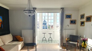 A living room with a sofa, two small tables, a chair, a chandelier, and a view of the outside. - MoMa Escape Kecskemét (Kecskemét)