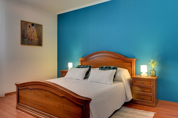 A bedroom with a wooden bed, two bedside tables, a nightstand, a lamp, and a vase with flowers. - Apartment with pool, air conditioning - to sandy beach 700 meters (Medulin)