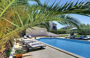 A swimming pool with lounge chairs, a palm tree, and a building in the background. - Apartment with pool, air conditioning - to sandy beach 700 meters (Medulin)