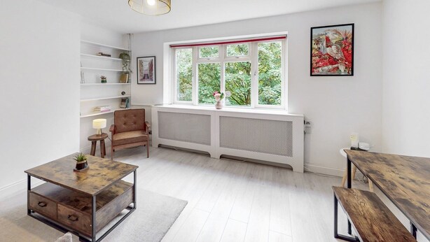 A bright, modern living room with a large window, a radiator, a wooden coffee table, a bookshelf, and a framed picture on the wall. - Stylish flat in West Hampstead - Pass the Keys (London)