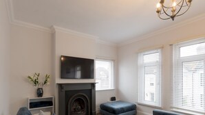 A modern living room with a fireplace, a flat-screen TV mounted above it, and a large window with blinds. - Cosy Flat in Leigh | Sea View - Pass the Keys (Southend-on-Sea)