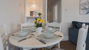 A dining area with a round table set for four, white chairs, and a vase with yellow flowers. - Cosy Flat in Leigh | Sea View - Pass the Keys (Southend-on-Sea)