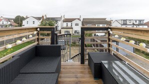 A wooden deck with black outdoor seating and a view of residential buildings in the background. - Cosy Flat in Leigh | Sea View - Pass the Keys (Southend-on-Sea)