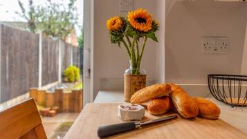 A wooden cutting board with a knife, a jar of cheese, and a bowl of bread on a kitchen counter.