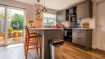 A modern kitchen with a central island, a built-in oven, and a large window overlooking a garden.