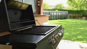An outdoor grill with a control panel, located in a backyard with a wooden fence and a lawn. - THE SABAYÉS VIEWPOINT (Sabayés)