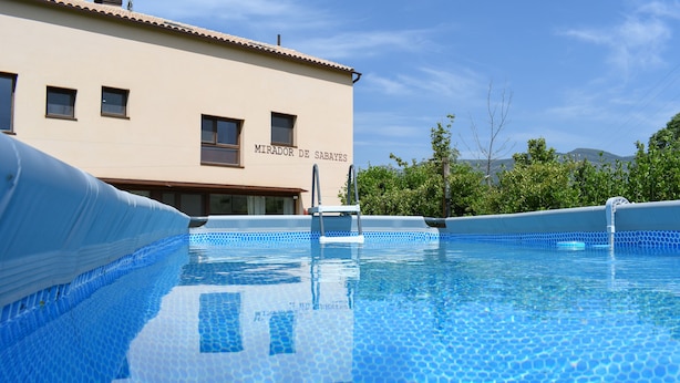A swimming pool with a tiled edge, a lifeguard stand, and a building with the sign "MIRADOR DE SABAYES" in the background. - THE SABAYÉS VIEWPOINT (Sabayés)