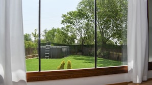 A room with a large window overlooking a backyard with a lawn, a tree, and a wooden fence. - THE SABAYÉS VIEWPOINT (Sabayés)