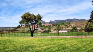 A grassy field with a tree and a fence, with buildings and mountains in the background. - THE SABAYÉS VIEWPOINT (Sabayés)