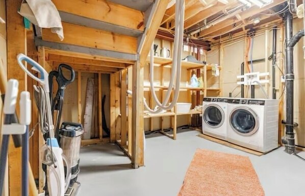 Un cuarto de lavado con lavadora, repisas con diversos objetos y vigas de madera a la vista.