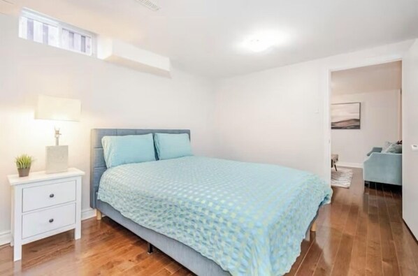 Un dormitorio con cama, mesita de noche, lámpara y una planta pequeña.