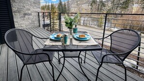 Une terrasse en bois avec une table et des chaises, deux assiettes de nourriture et un vase de fleurs.