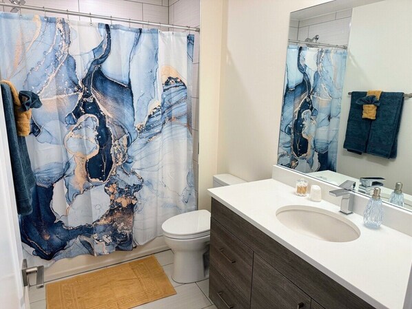 A bathroom with a marble-patterned shower curtain, a white toilet, a white sink with a mirror above it, and wooden cabinets.
