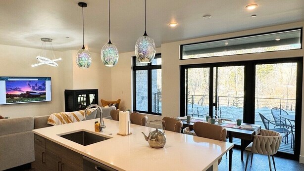 Une cuisine moderne dotée d’un grand îlot central, de luminaires suspendus et d’un coin repas avec des chaises et une table.